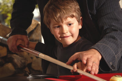 Adult helping child learn how to play pool