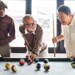 Three friends enjoying a game of pool together, showing the long-lasting joy of a quality billiard table available at Skillful Home in Portland, Maine