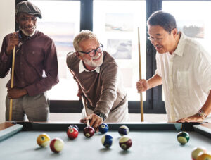 Three friends enjoying a game of pool together, showing the long-lasting joy of a quality billiard table available at Skillful Home in Portland, Maine
